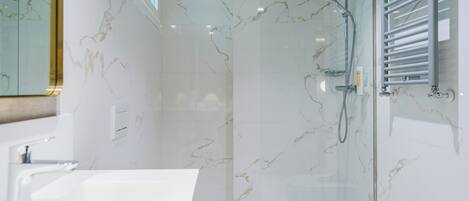 Un baño moderno con ducha envuelta en vidrio, lavamanos blanco y retrete.