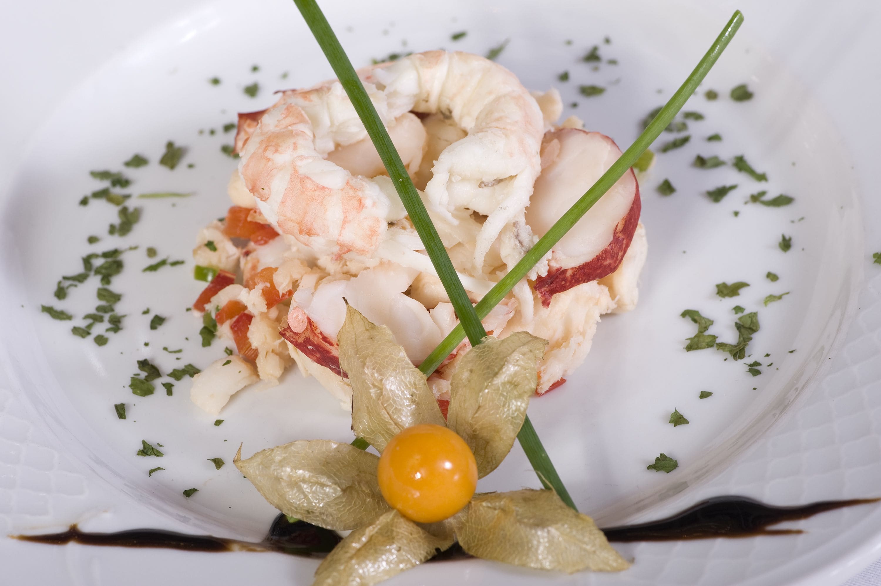 Un plato de mariscos, adornado con hierbas verdes y una flor comestible amarilla.