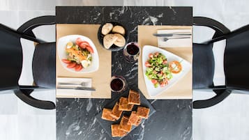 Una mesa de comedor con dos platos de ensalada, una cesta de pan y dos copas de vino tinto.