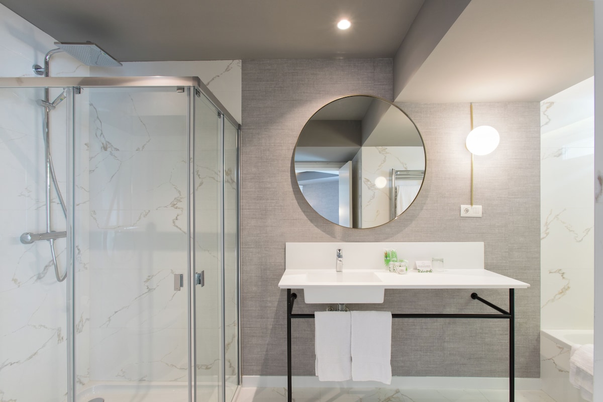 A modern bathroom with a glass shower enclosure, a white sink with a mirror above it, and a towel rack with two white towels.