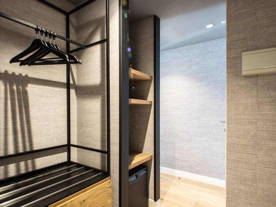 Habitación moderna y compacta con cama integrada, suelo de madera y estantería montada en la pared.