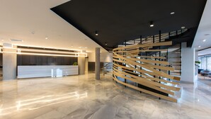 A modern lobby with a curved wooden staircase, a reception desk, and a marble floor. - Hotel Riazor (A Coruña)