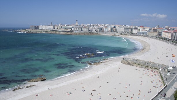 A coastal cityscape with a wide beach, clear blue waters, and a prominent tower. - Hotel Riazor (A Coruña)