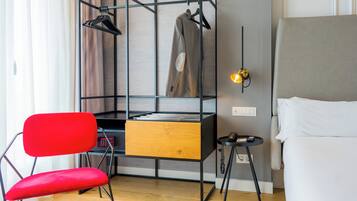 A modern room with a bed, a red chair, a desk with a hanging coat rack, and a small table with a phone.