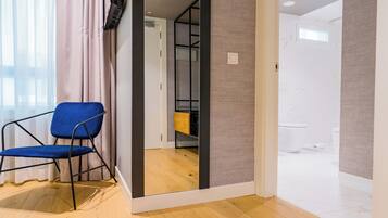 Una habitación con una silla azul, suelo de madera, un espejo y vistas al baño.