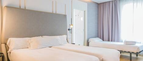 A hotel room with two beds, a nightstand, a lamp, a window with curtains, and a door.