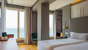 A hotel room with a large bed, a desk, a chair, and a view of the sea. - Hotel Riazor (A Coruña)