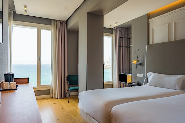 A hotel room with a large bed, a desk, a chair, and a view of the sea.