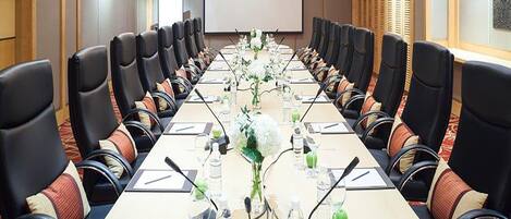 A conference room with a long table, multiple chairs, and a projector screen.