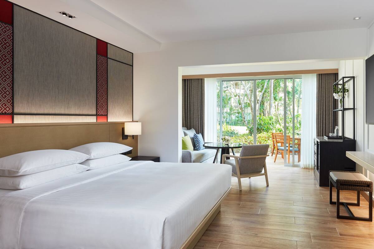 Ein Hotelzimmer mit einem großen Bett, einem Schreibtisch, einem Stuhl und Blick ins Freie.
