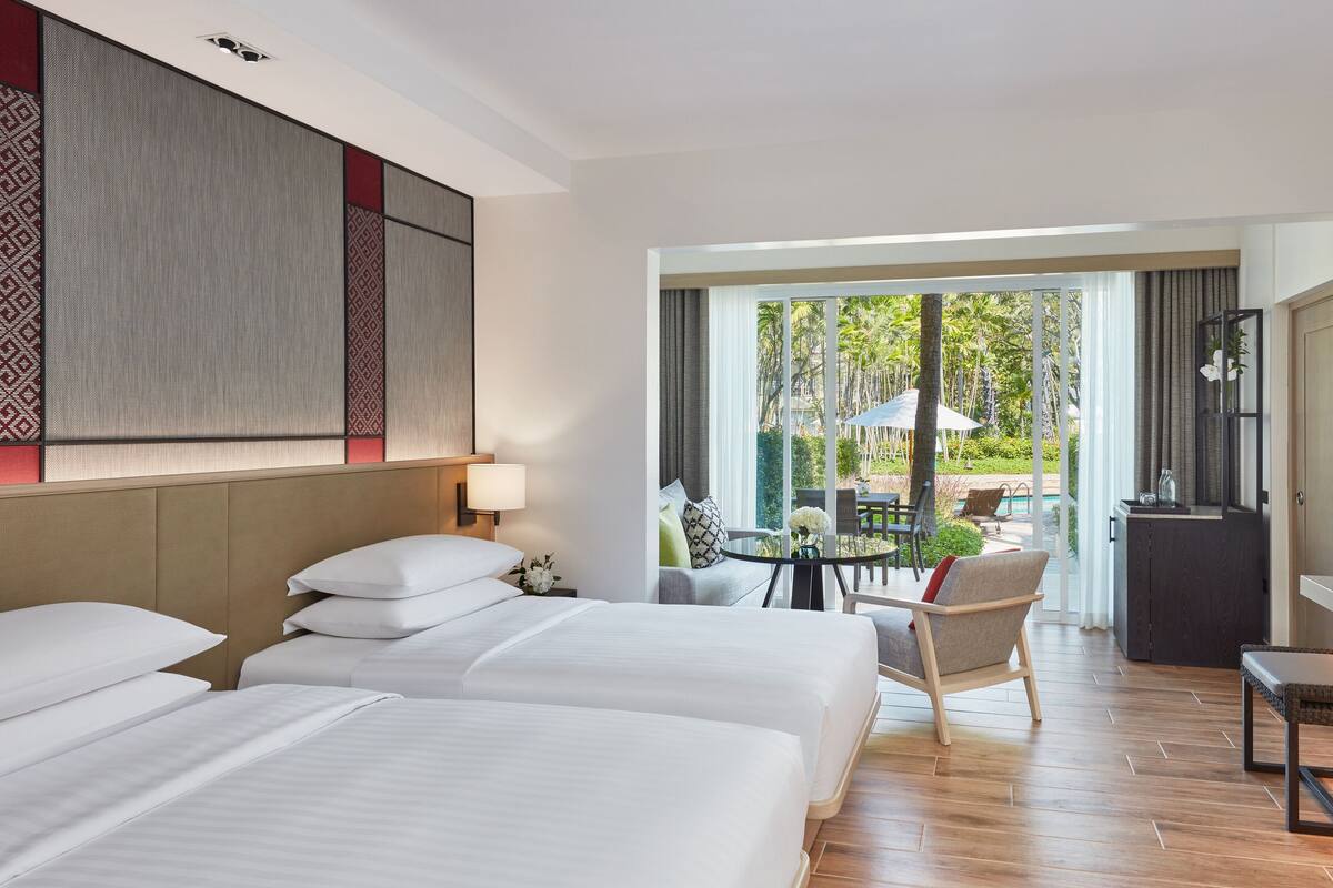 Ein Hotelzimmer mit zwei Betten, einer Essecke mit Tisch und Stühlen sowie Blick ins Freie.