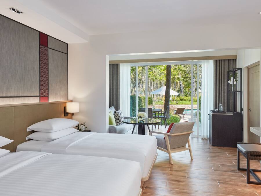 A hotel room with two beds, a dining area with a table and chairs, and a view of the outdoors.