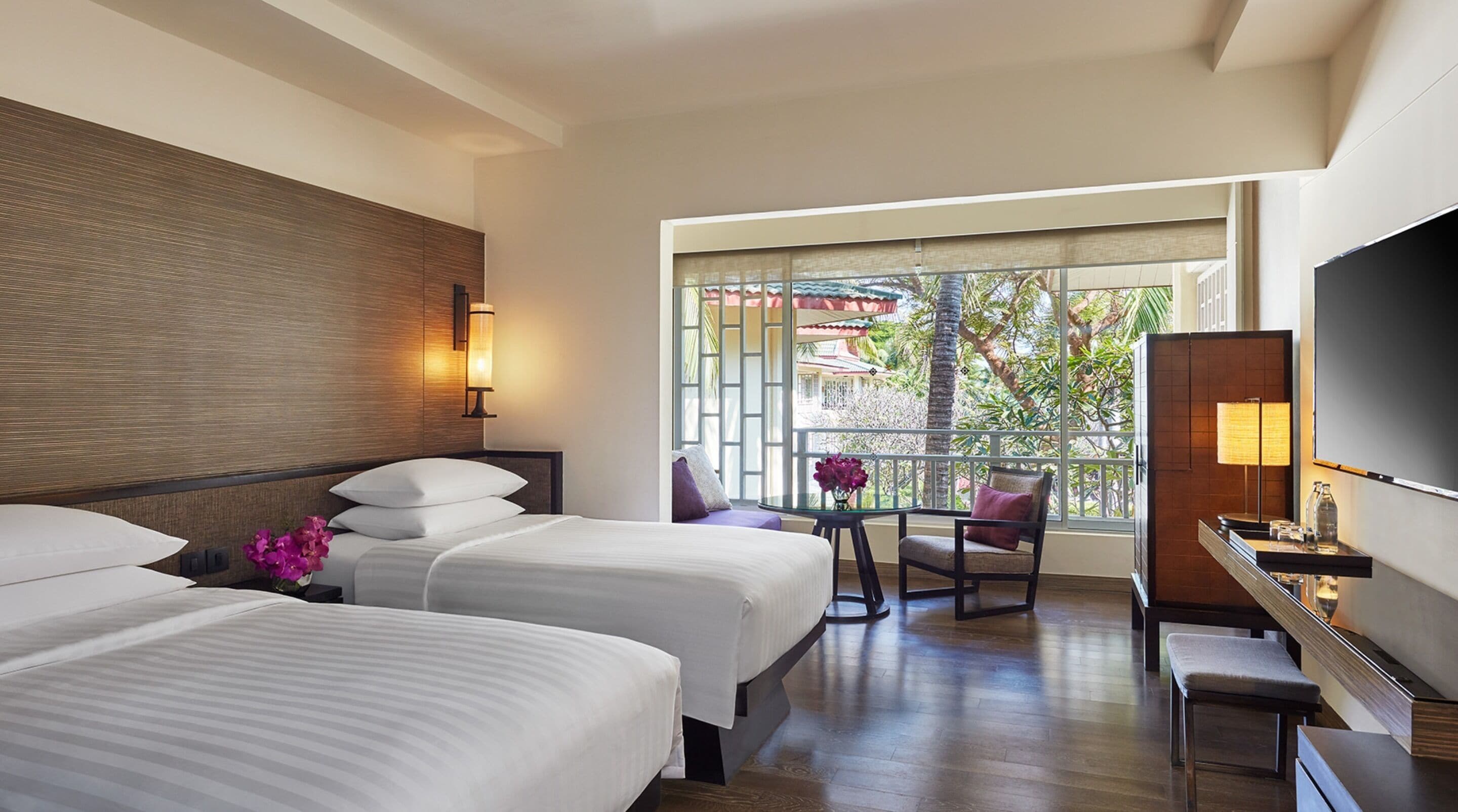 A hotel room with two beds, a balcony with a view, a desk, and a TV.