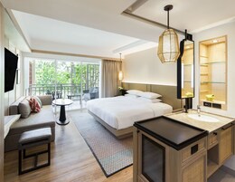 Una habitación de hotel moderna con cama, sofá, mesa de comedor y un balcón con vista a zonas verdes.