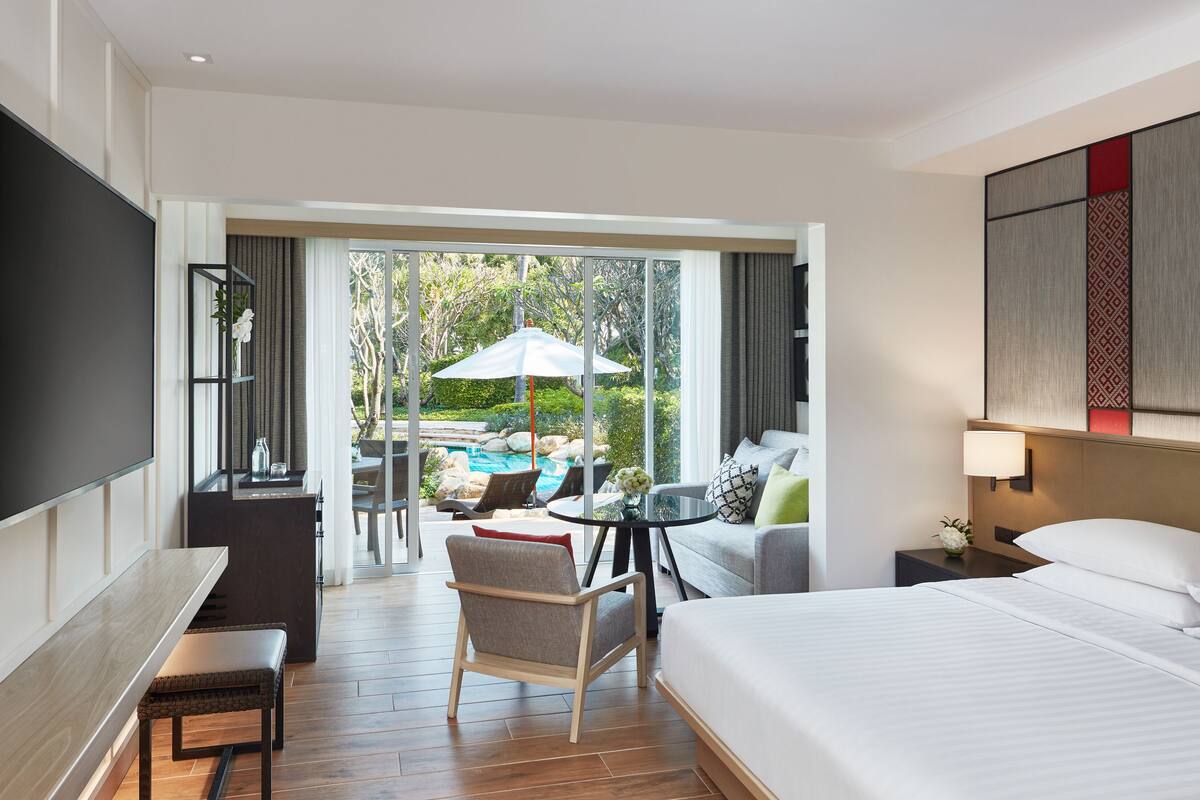Ein Hotelzimmer mit Bett, Schreibtisch, Stuhl, Fernseher, Nachttisch und Blick auf einen Außenpool.