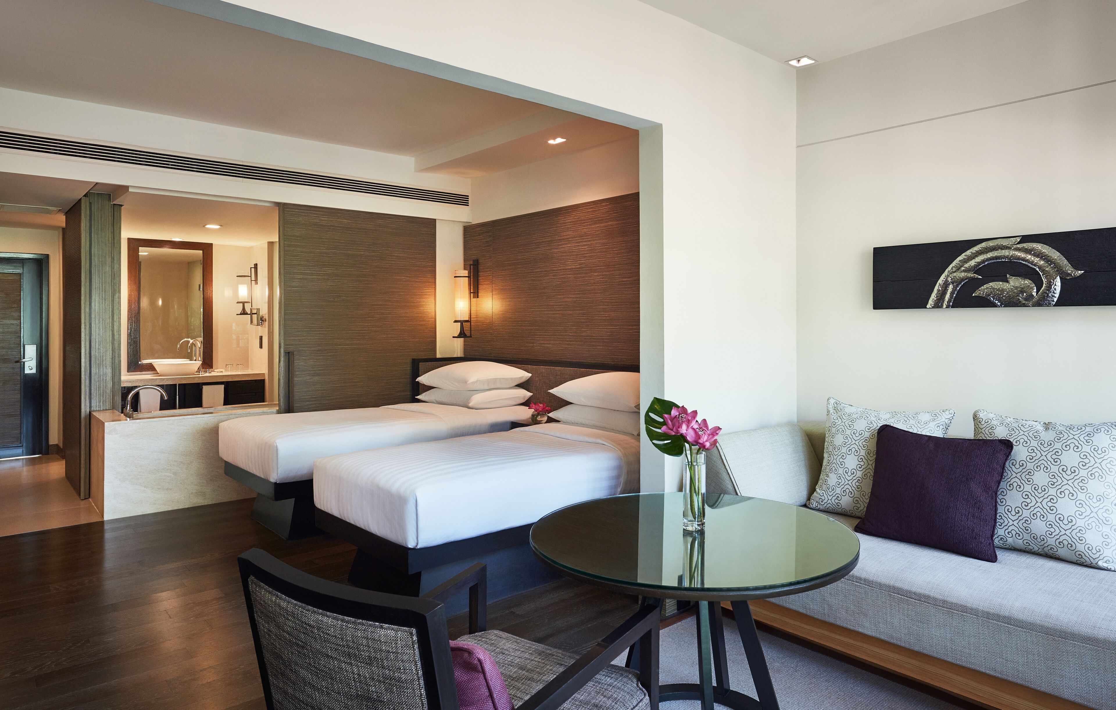 Una habitación de hotel con cama, sofá, una mesita de cristal y baño a la vista a través de una puerta abierta.