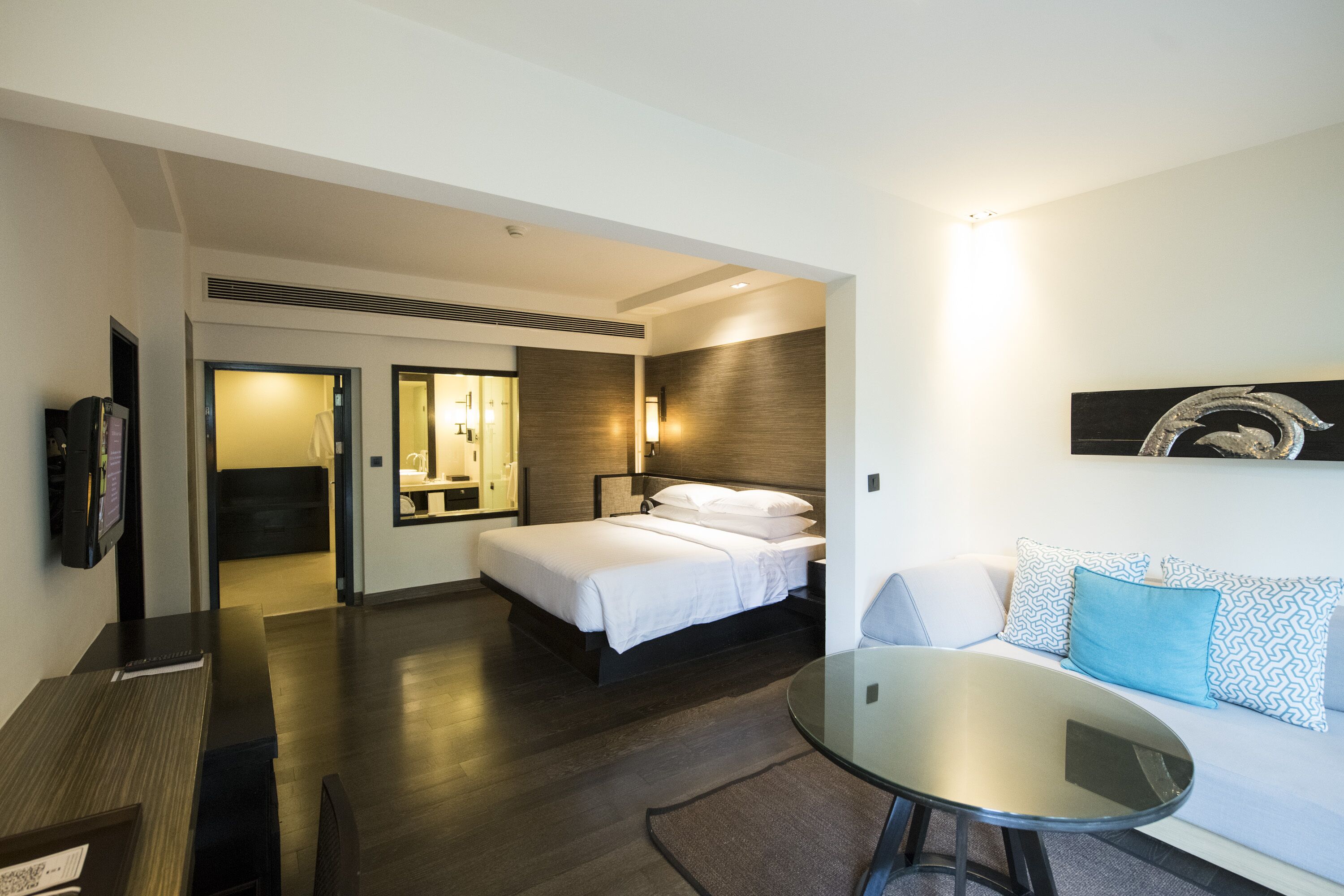 A modern hotel room with a bed, a sofa, a glass table, and a TV.