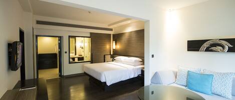 A modern hotel room with a bed, a sofa, a glass table, and a TV.
