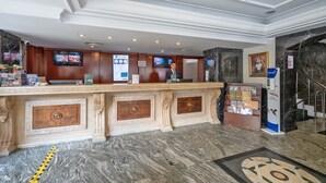 Uma área de recepção com piso de mármore, balcão de atendimento com tela digital e escada com parede revestida em mármore.