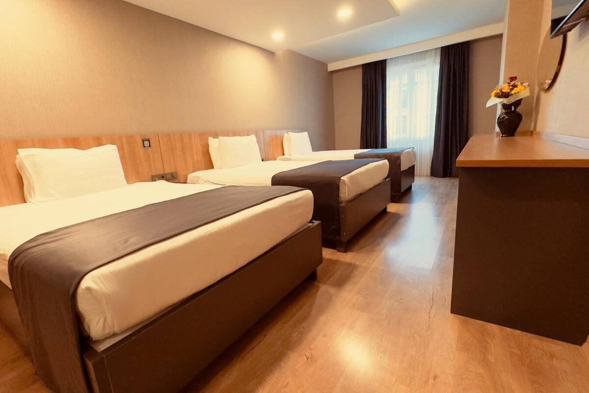 A hotel room with two beds, a small desk, and a vase with flowers.