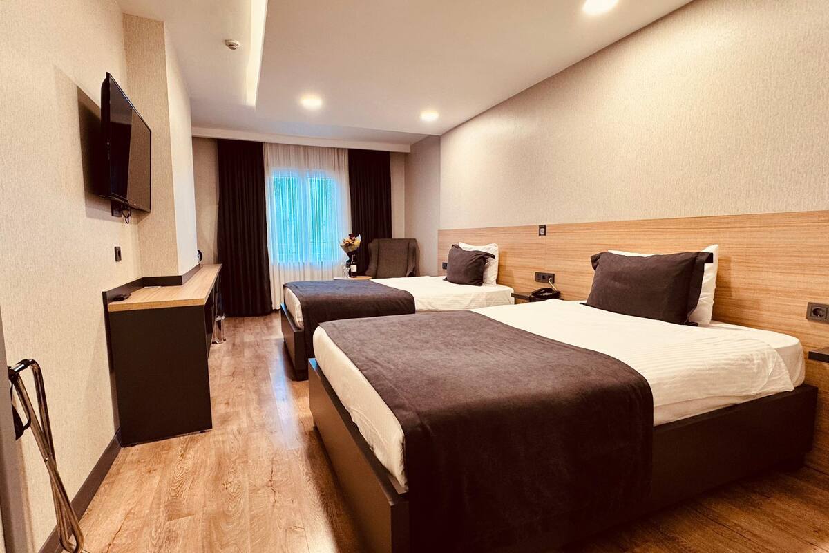 A hotel room with two beds, a desk, a TV, and a window with curtains.
