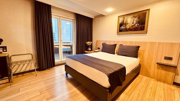 Quarto de hotel com uma cama grande, uma escrivaninha com cadeira, um quadro na parede e vista pela janela.