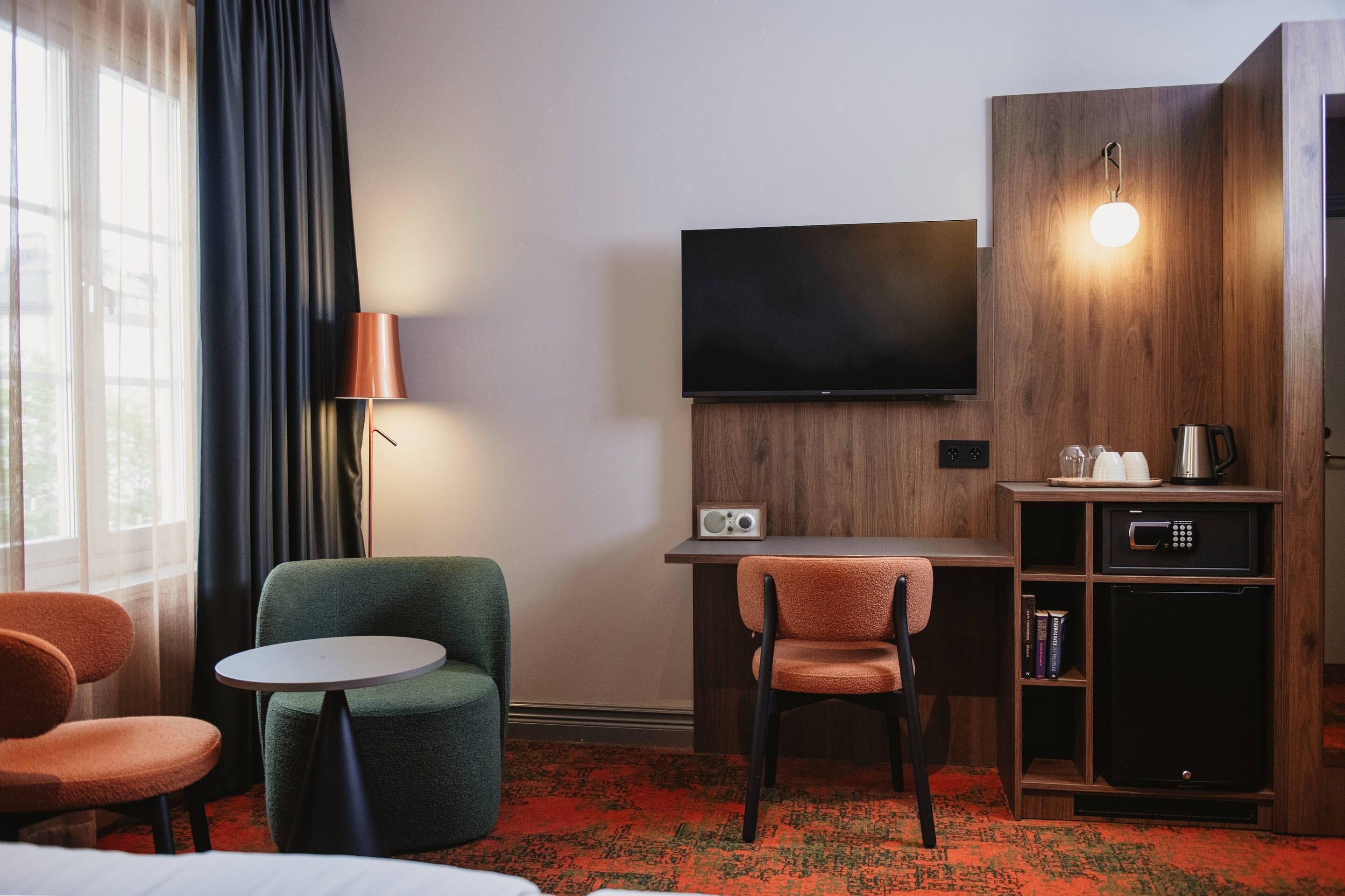 Ett hotellrum med en säng, ett skrivbord med en stol, en tv, en lampa, en mikrovågsugn och en kaffebryggare.