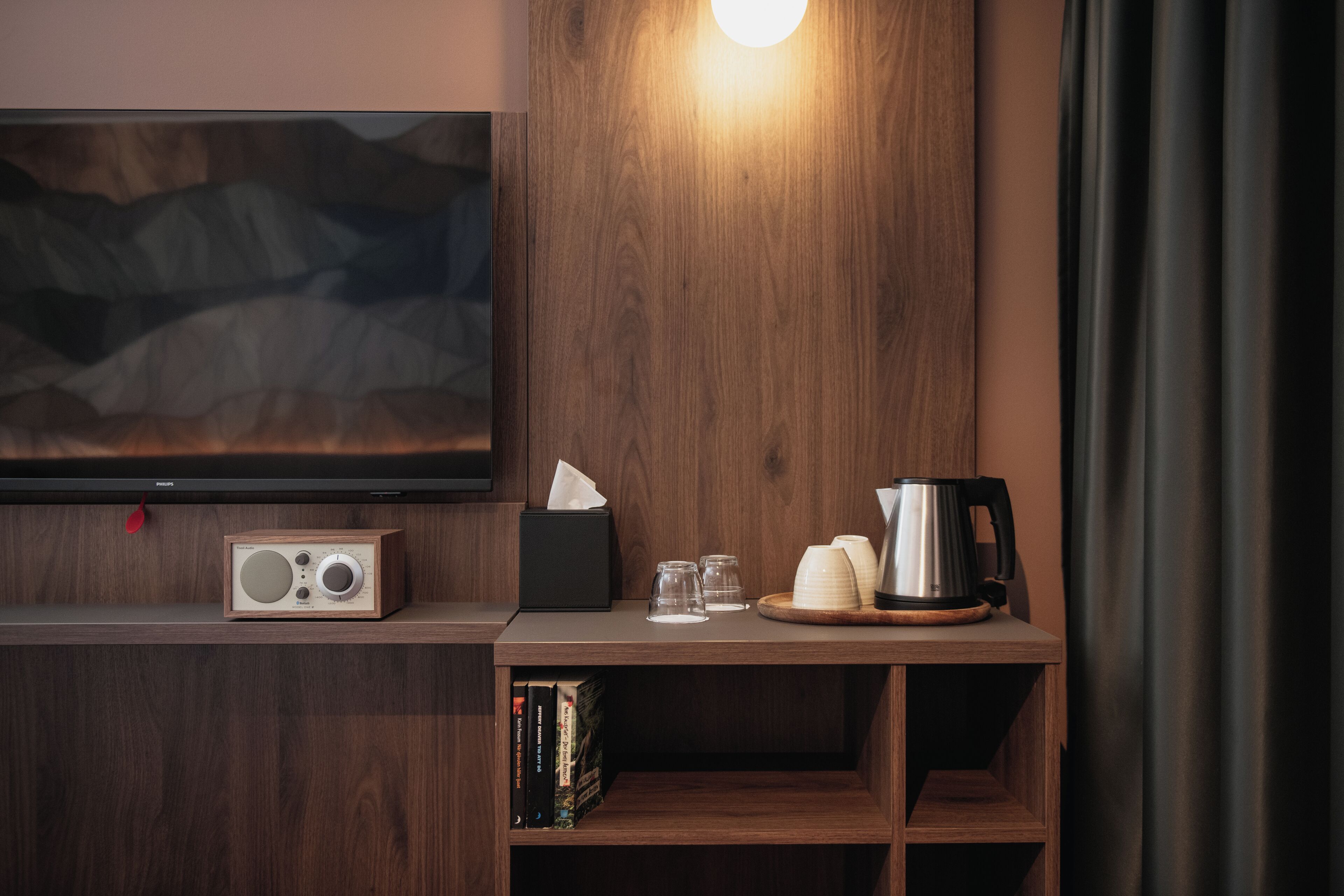 Una habitación moderna con un mueble bajo de madera para el televisor, una radio, una cafetera y una estantería con libros.