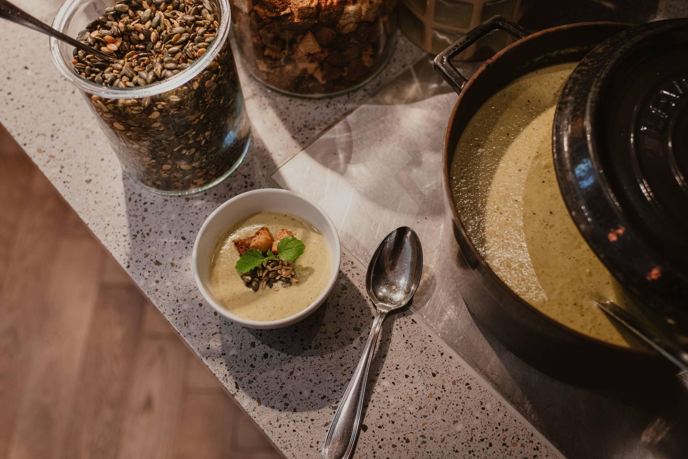A bowl of soup with seeds and a spoon on a speckled countertop.