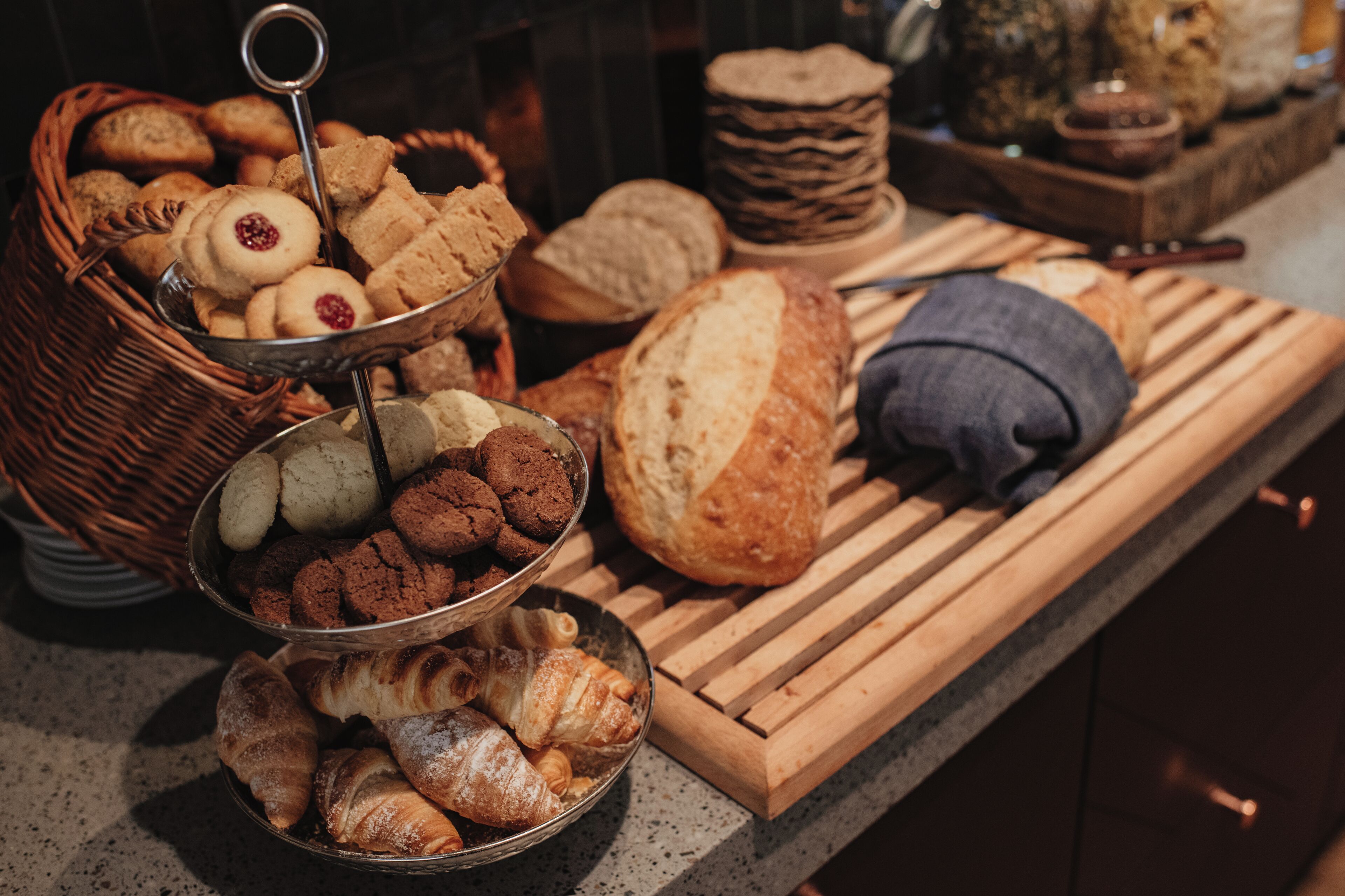 Une variété de produits de boulangerie, notamment du pain, des croissants et des biscuits, présentés sur une planche en bois et dans un plateau en métal.