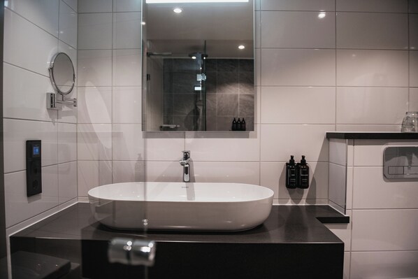 Un baño moderno con un lavabo grande de color blanco, un espejo y una zona de ducha.