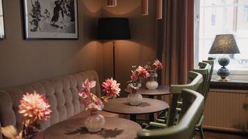 A cozy room with a sofa, two small round tables with vases of flowers, a lamp, and a view of the outside through a window.