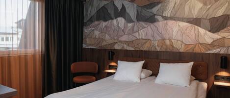 Una habitación de hotel con una cama, una silla, un escritorio y una pared con un diseño de montaña.