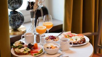 A breakfast table with various dishes, drinks, and a vase with dried flowers.