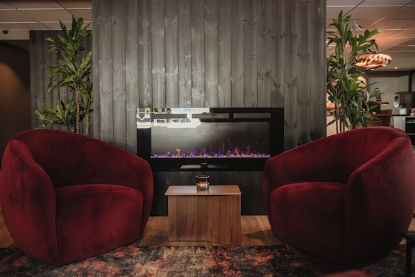 A modern living room with a flat-screen TV, two red velvet armchairs, a small wooden coffee table, and a decorative plant.