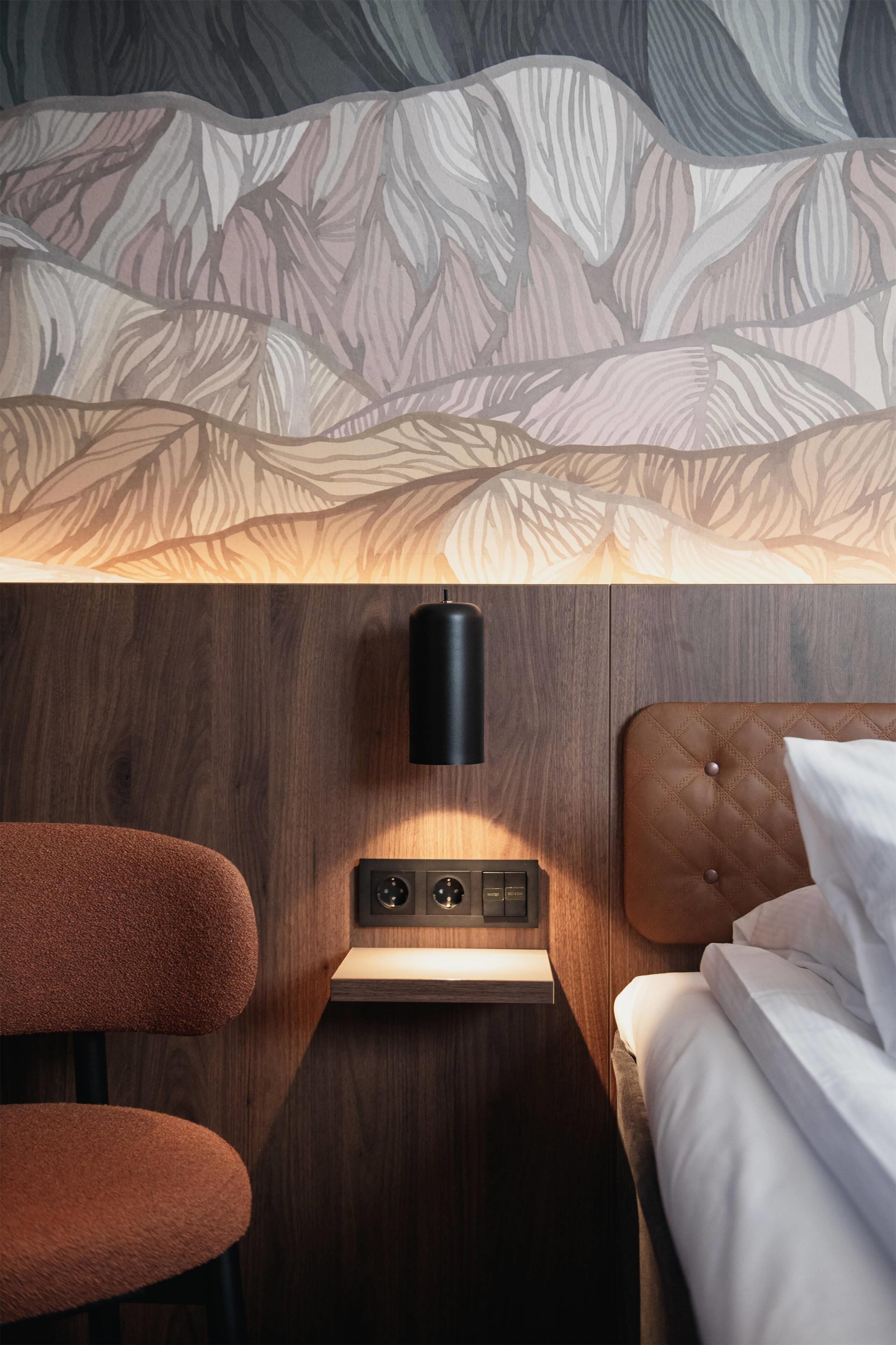 A bedroom with a bed, a nightstand with a lamp, and a chair.