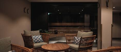 A modern lounge area with wicker furniture, a round wooden table, and a glass partition.