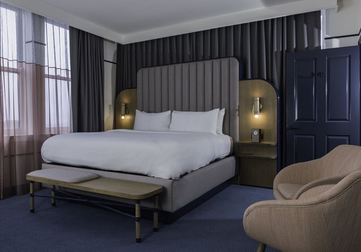 Una moderna camera d'albergo con un letto grande, comodini, una panca e una sedia.