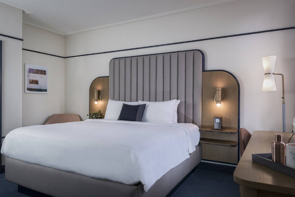 Una habitación de hotel con una cama grande, mesitas de noche, un escritorio y una silla.
