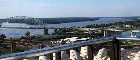 A balcony with a view of a river, a bridge, and a distant cityscape.