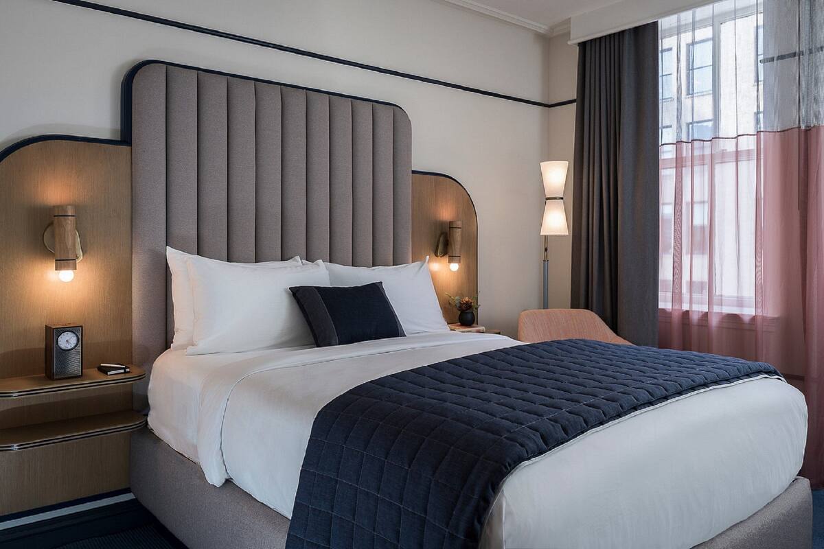 Una habitación de hotel moderna con una cama grande, dos mesitas de noche, un reloj y una lámpara.
