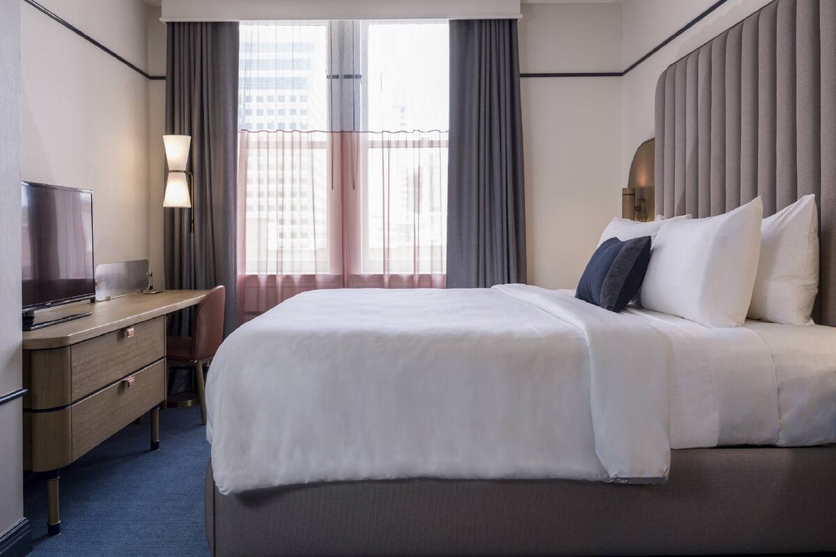 Una habitación de hotel con una cama grande, un escritorio con una silla, un televisor y una ventana con cortinas.