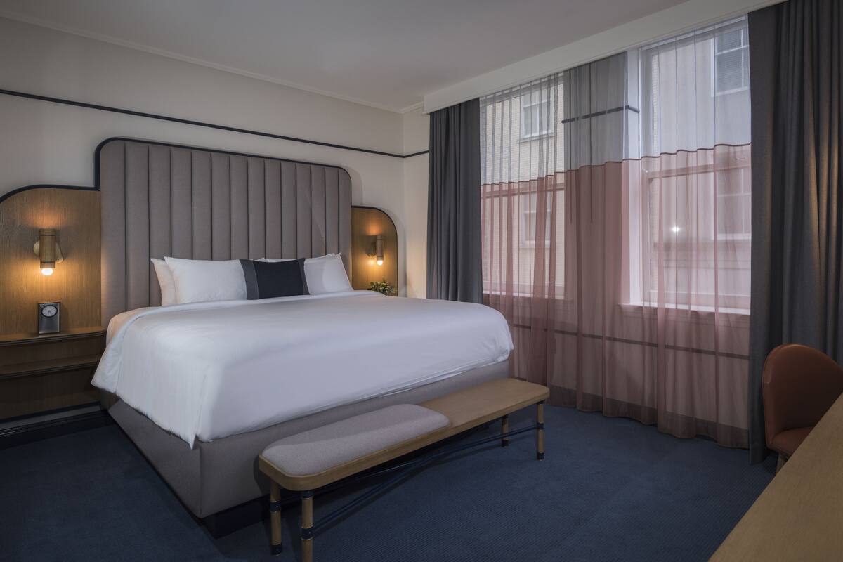 Una habitación de hotel con una cama grande, lámparas de noche, un escritorio y una silla.