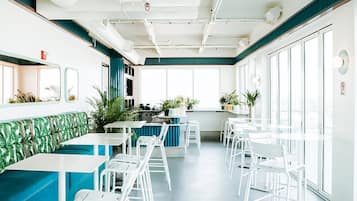 A spacious indoor area with a long counter, white chairs, and tables, and large windows allowing natural light.