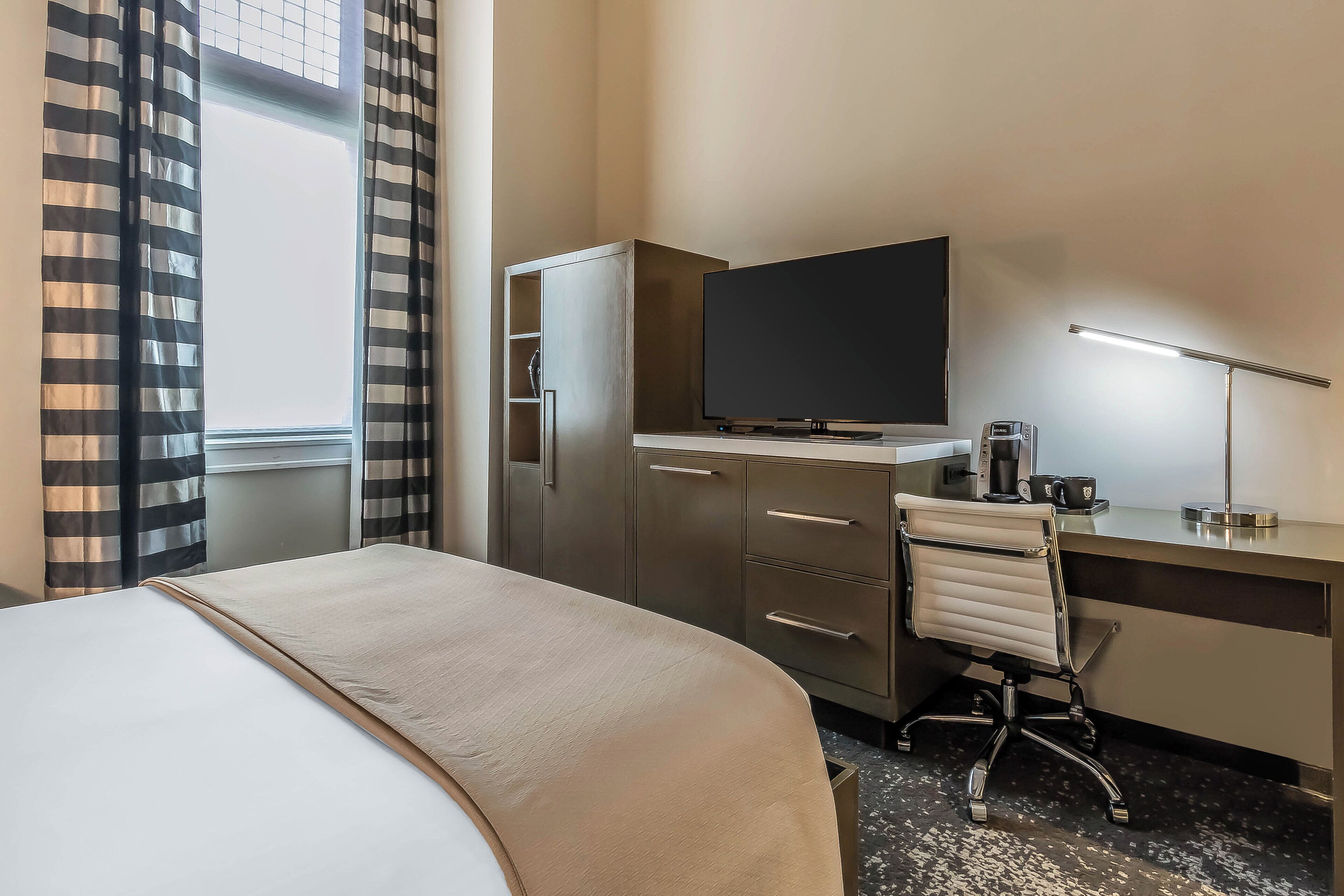 A hotel room with a bed, a desk with a computer, a TV, and a coffee maker.