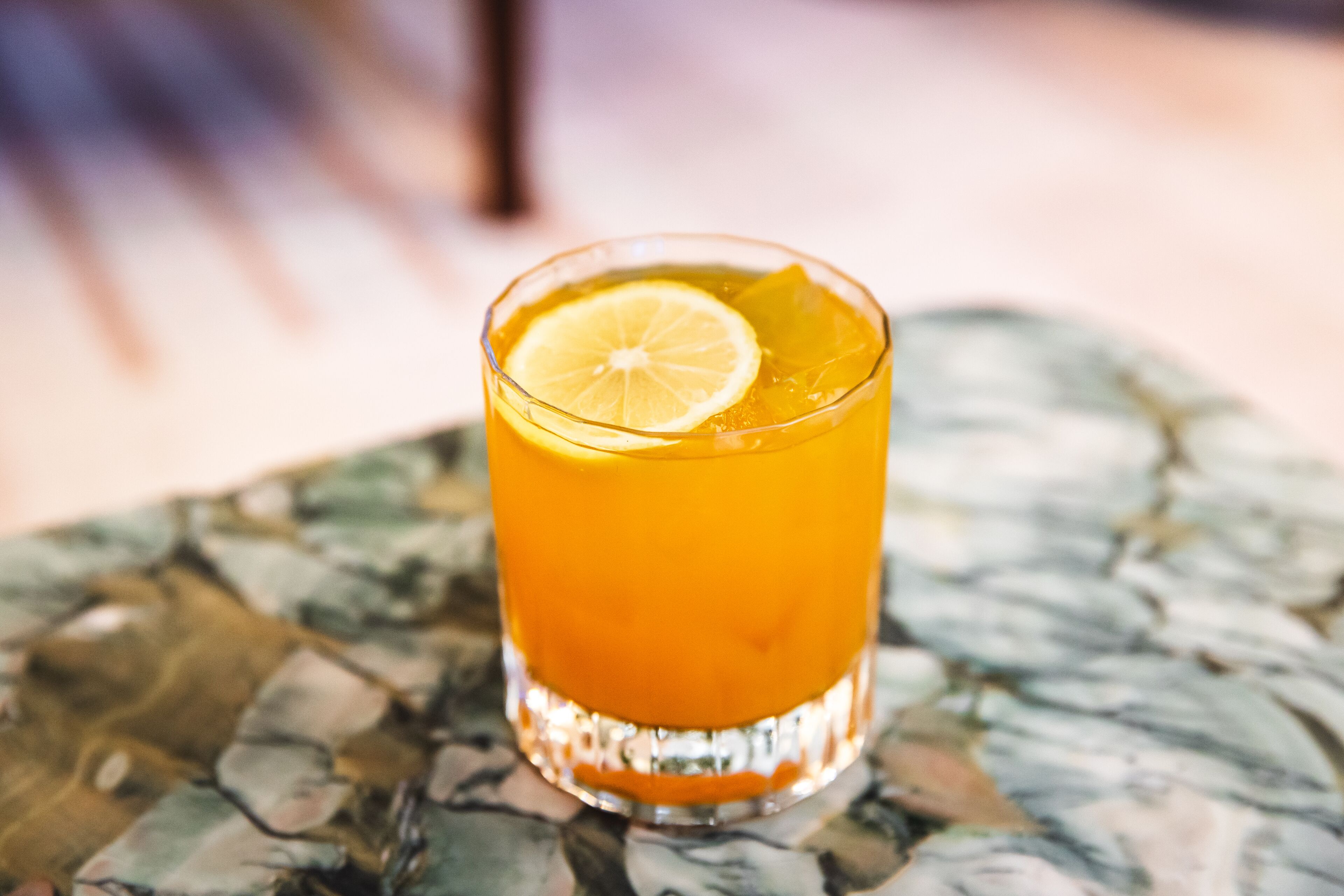 Un vaso de jugo de naranja con una rodaja de limón sobre una mesa con diseño de mármol.