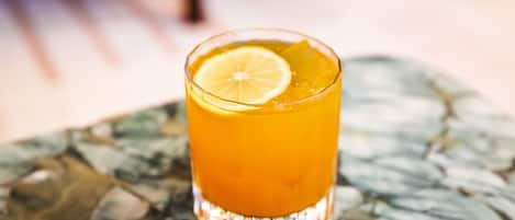 A glass of orange beverage with a lemon slice on a table with a marble pattern.