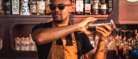 Ein Barkeeper mischt Getränke hinter der Bar, umgeben von verschiedenen Flaschen und Gläsern.