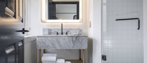 Un baño moderno con un lavabo de mármol, un espejo con iluminación trasera y una zona de ducha.