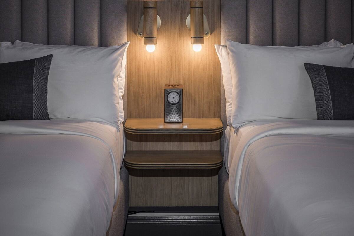 Un dormitorio con dos camas, una mesita de noche con un reloj e iluminación en la pared.